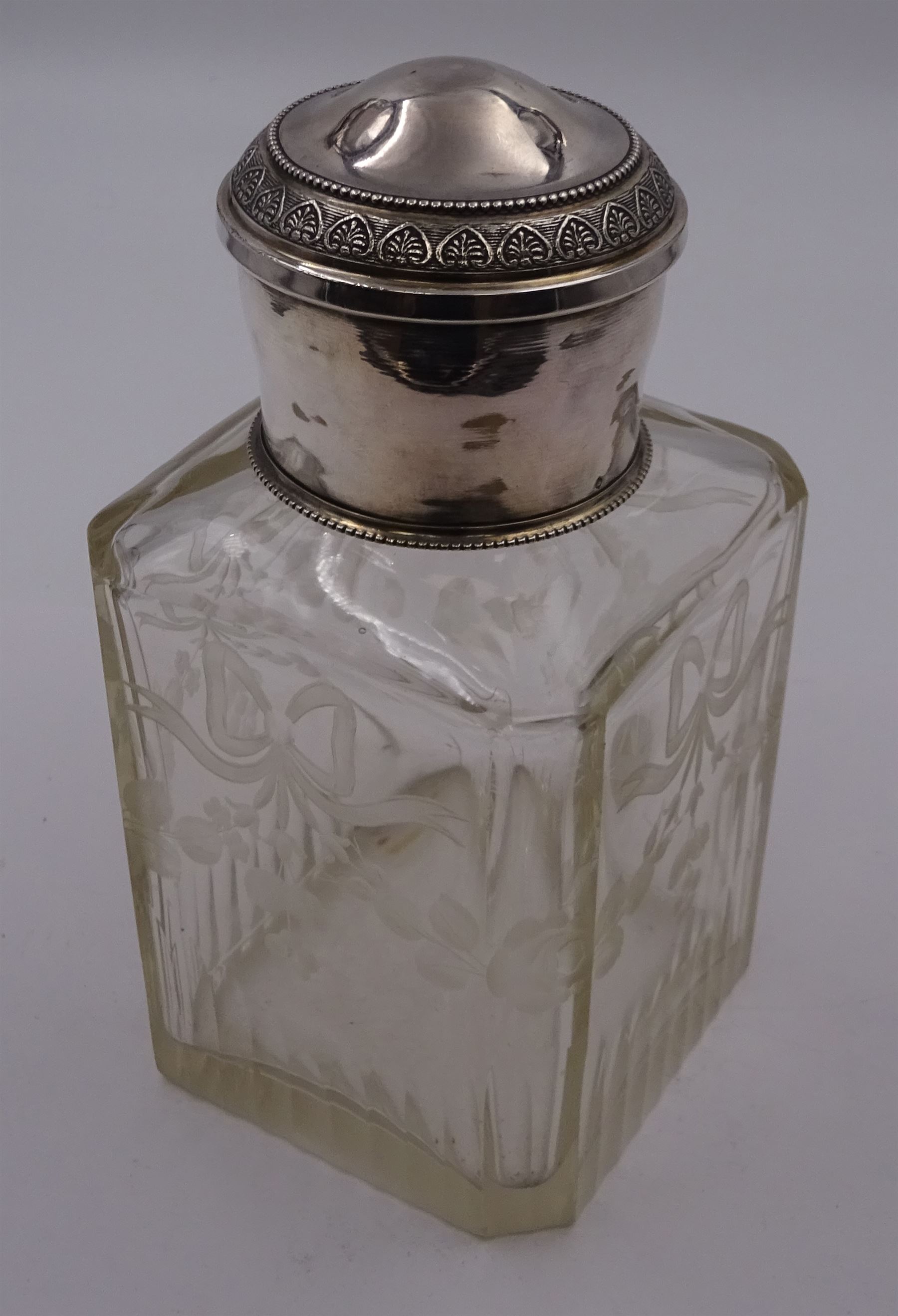 Early 20th century French silver mounted glass scent bottle, the faceted rectangular glass body etched with swags of flowers united by ribbons, with cylindrical silver cover embossed with foliate detail and beaded decoration with gilt interior, marked with Minerva's head, with white metal collar and glass stopper, H17cm