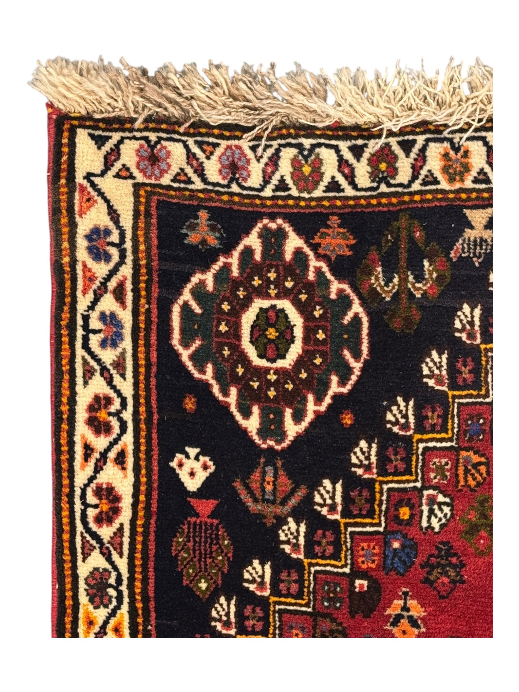 Persian Qashqai crimson ground runner, the field decorated with repeating diamond-shaped medallions flanked by angular floral motifs, the spandrels with intricate boteh designs, framed by an ivory border with stylised floral patterns and scrolling vines