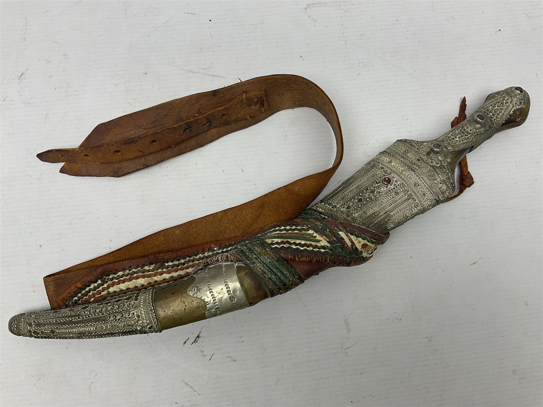 Saudi Arabian khanjar dagger with 29.5cm curving double edged  steel blade; white metal and copper mounted horn grip; in white metal mounted brass and leather scabbard incorporating embroidered leather wearing strap