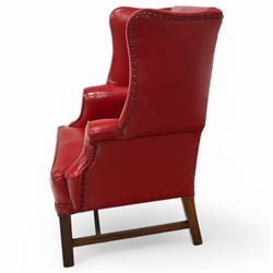 20th century Georgian design mahogany framed wingback armchair upholstered in red leather, shaped back flanked by winged sides and down-swept arms raised on squared legs 