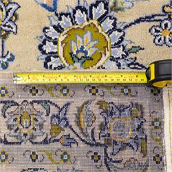 Central Persian Kashan hand-knotted carpet, pale ivory ground, decorated with an all-over scrolling floral design of palmettes rosettes, and leafy vine work enclosed by a wide floral border and multiple guard borders in tones of soft blues, sage green, muted gold, and ivory, with cotton fringe ends