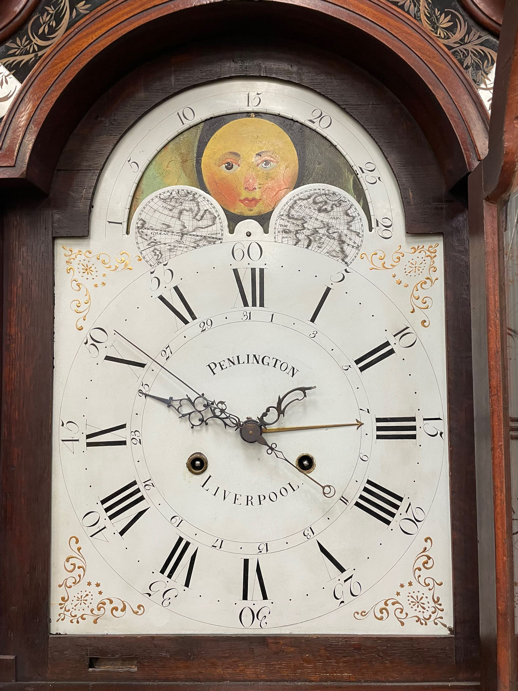 Penlington of Liverpool – early 19th century 8-day mahogany longcase clock, swans neck pediment with three turned wooden finials and verre eglomise panels, trunk with reeded columns and wavy topped door, plinth with canted corners on bracket feet, painted break-arch dial with Roman numerals and five-minute Arabic’s, centre sweep calendar and seconds hands, blue steel serpentine hands, signed beneath a painted rolling moon in the arch PENLINGTON, LIVERPOOL, eight day four pillar movement, anchor escapement and rack striking on a bell. With pendulum and weights.  The Penlington family were prolific clockmakers in 19th century Liverpool working from several addresses in the city, also recorded as chronometer and chronograph makers.