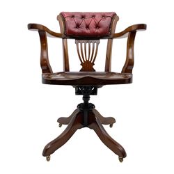 Early 20th century walnut swivel desk elbow chair, deeply button upholstered back in red leather over vase shaped pierced splat, dished saddle type seat, adjustable metal mechanism, on four splayed supports with brass castors