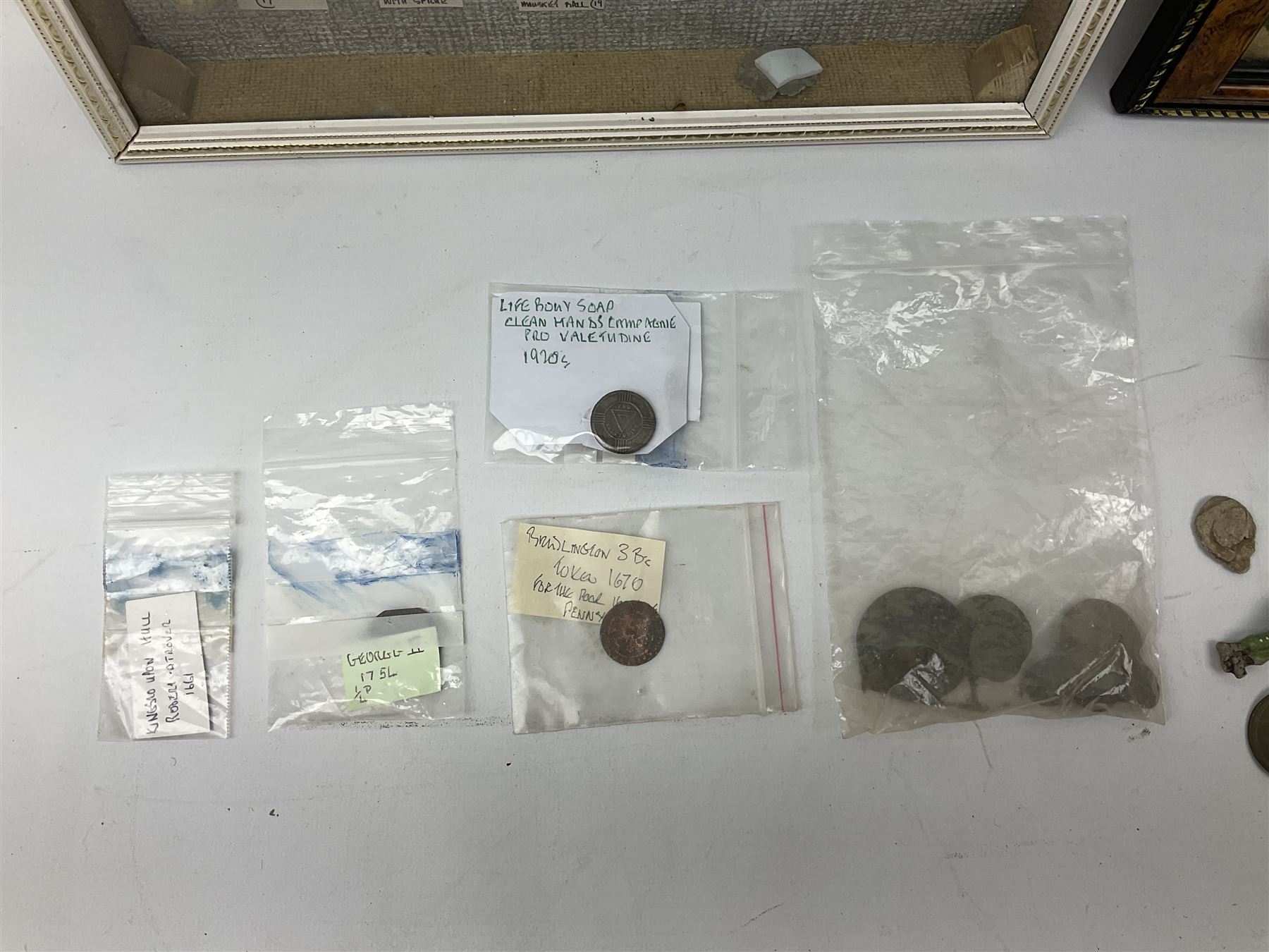 Collection of metal detecting finds, most contained within display frames and labelled, some loose, to include musket balls, bill hook, axe fragment, hubcaps, shell cases, regimental badges, coins, etc. 