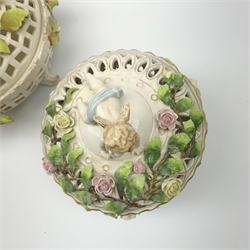 A Schierholz porcelain pot pourri basket and cover, c.1900, the pierced body raised upon three scroll feet, encrusted with vines and flowers and surmounted by a cherub with harp, with printed mark beneath, H21cm, together with another similar smaller Schierholz example. (2). 