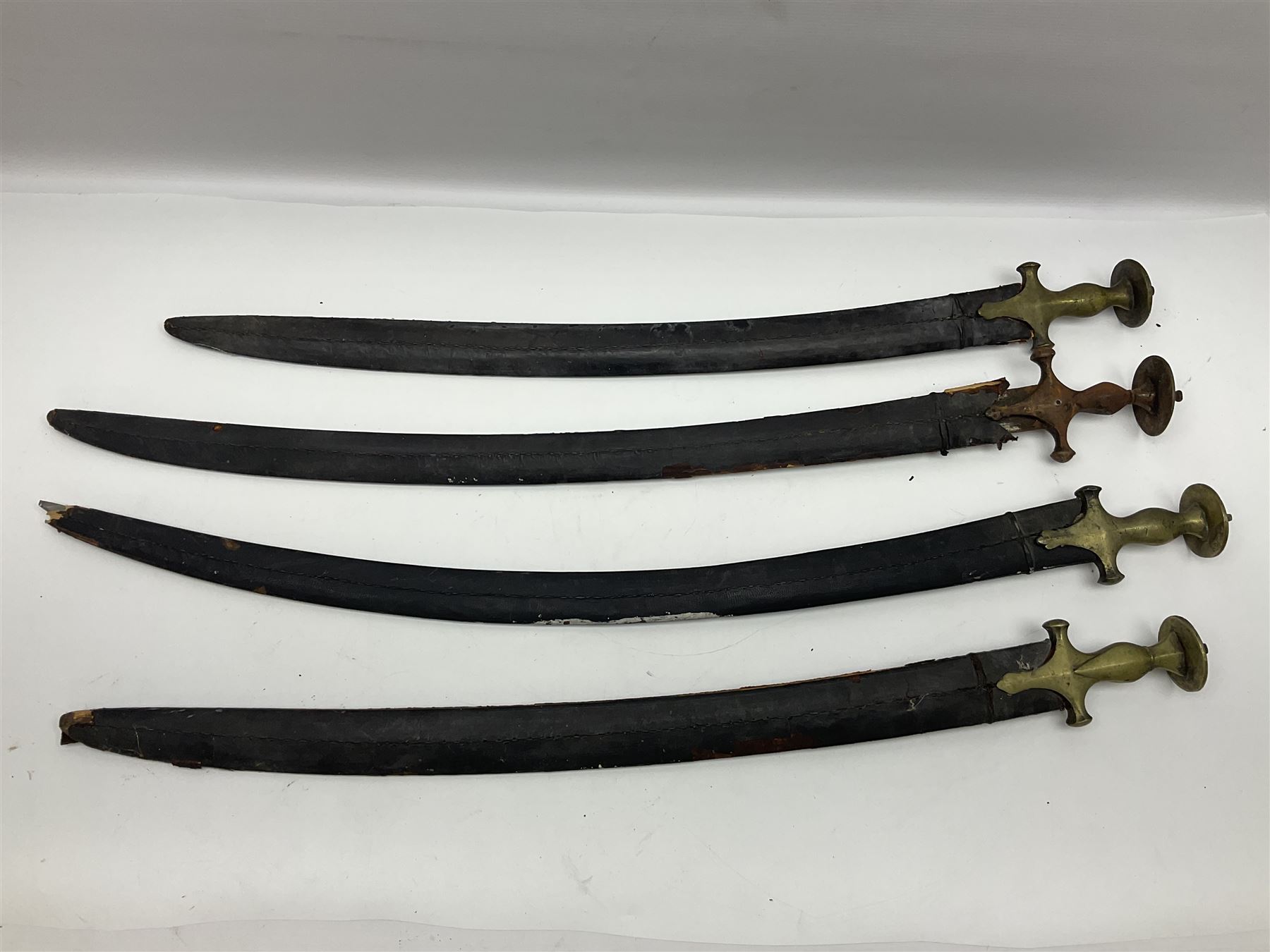Four Indian tulwar swords; three with cast brass hilts and one with iron hilt; longest blade 81cm; all with scabbards (4)