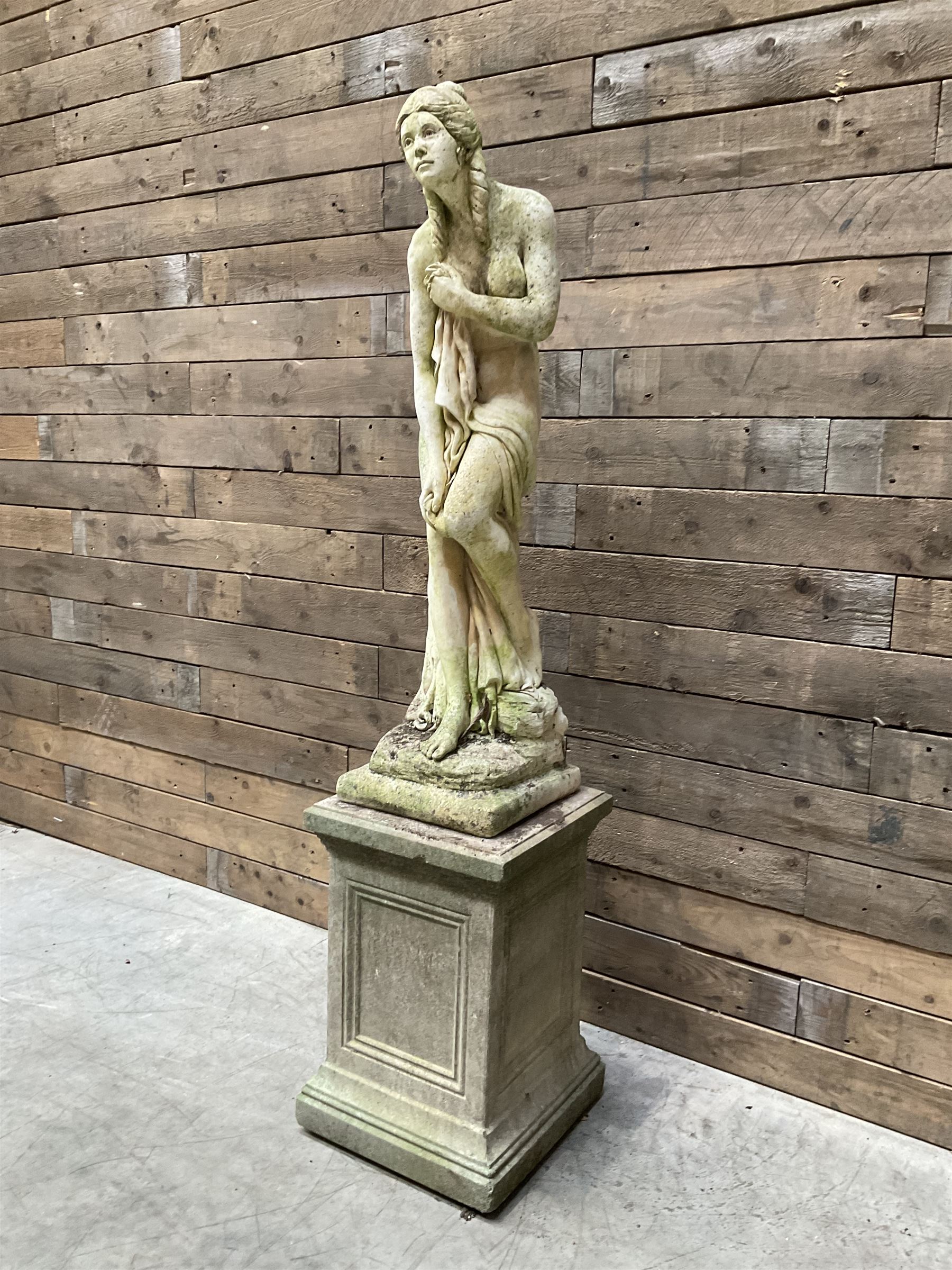 Cast stone garden figure of a bathing lady, raised on square plinth