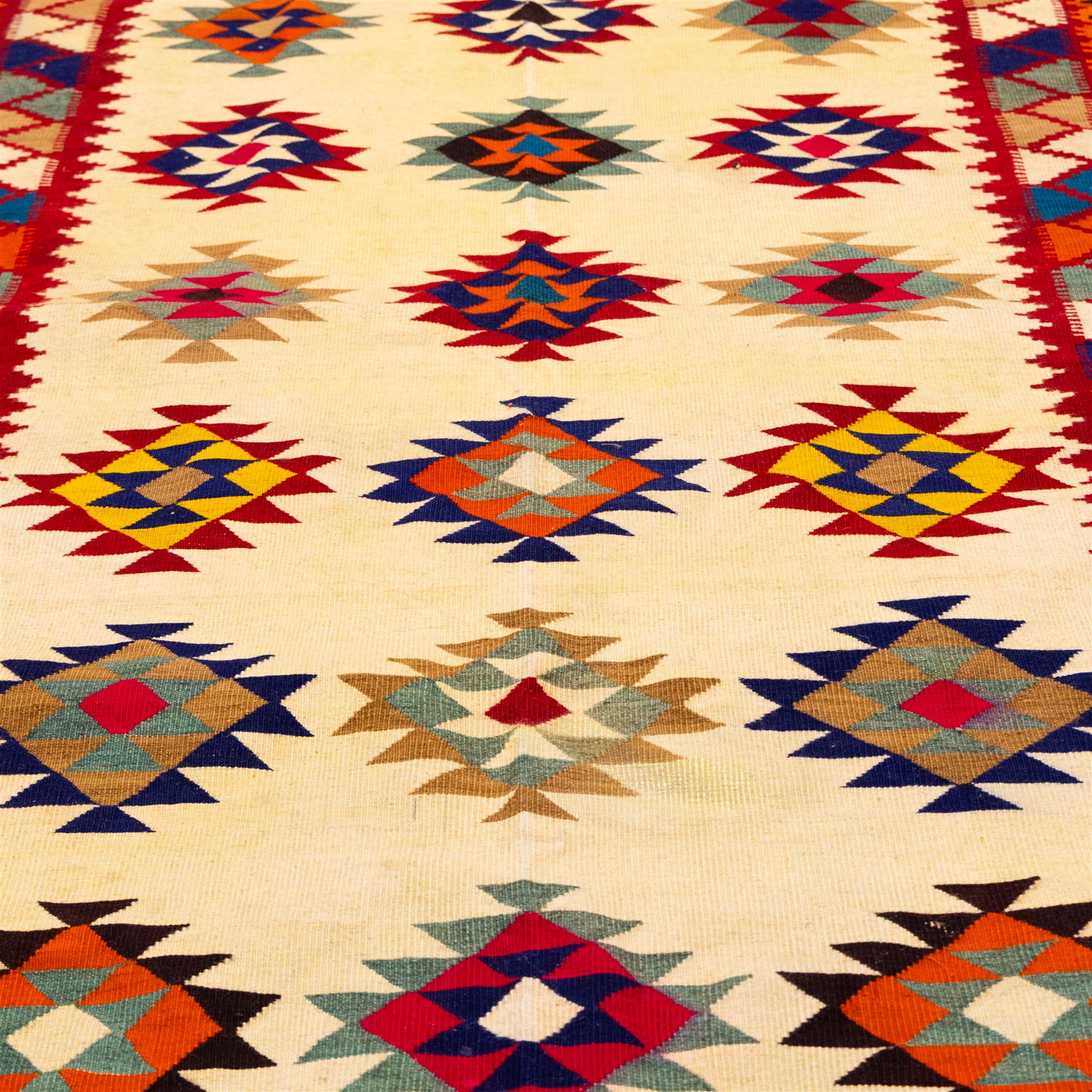 South West Persian Qashqai flatweave kilim, ivory field decorated with rows of multicoloured stepped diamond medallions composed of angular geometric motifs, enclosed by bold polychrome borders of triangular devices and stylized geometric, ornamentation, with fringe ends 