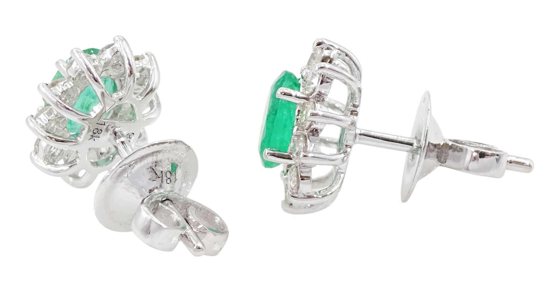 Pair of 18ct white gold emerald and diamond cluster earrings, each stud set with a single oval cut emerald surrounded by round brilliant cut diamonds, stamped, total emerald weight approx 0.90 carat, total diamond weight approx 0.60 carat