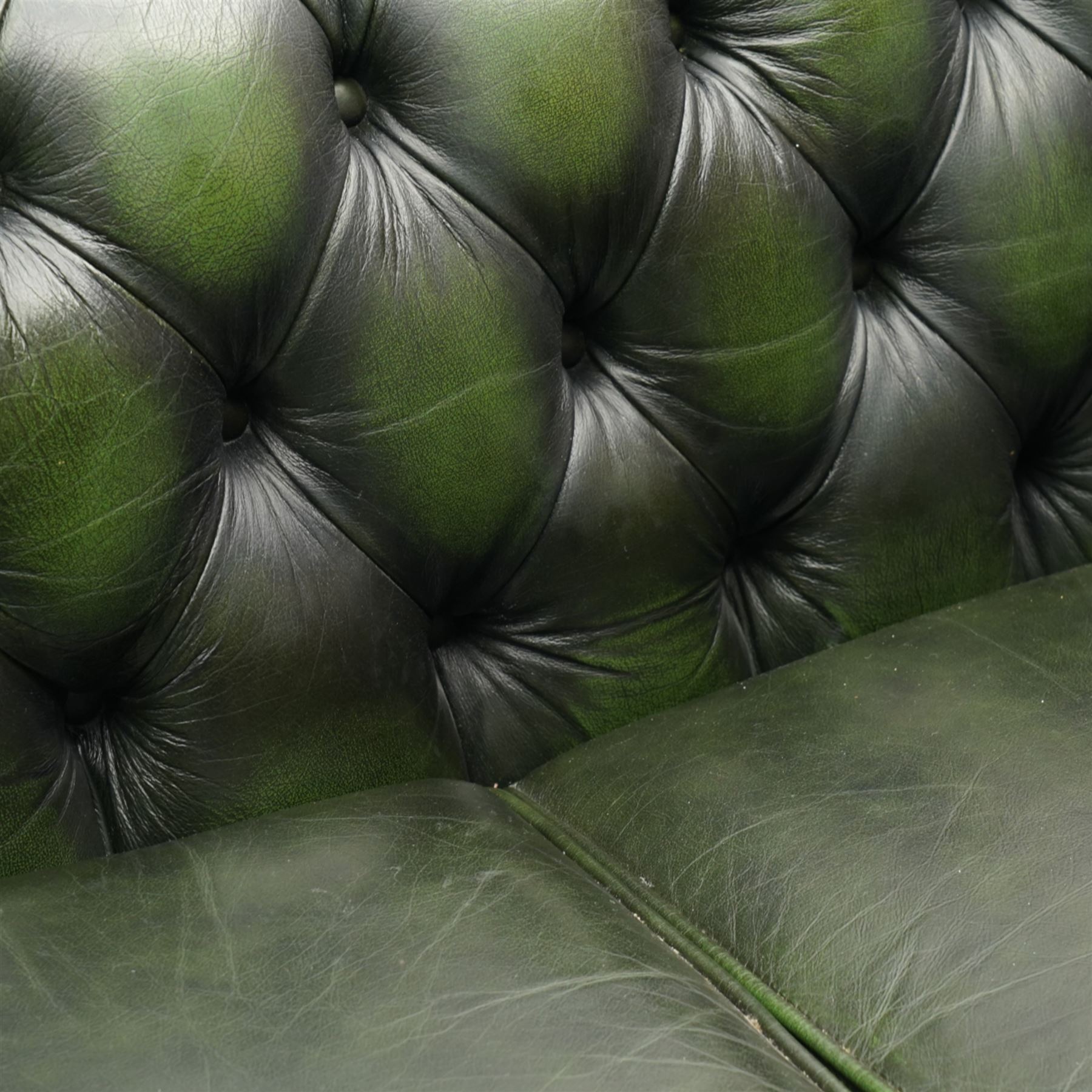 Thomas Lloyd - two-seat hardwood-frame Chesterfield sofa, traditional rolled back and arms upholstered in deeply buttoned green leather, on turned bun feet 