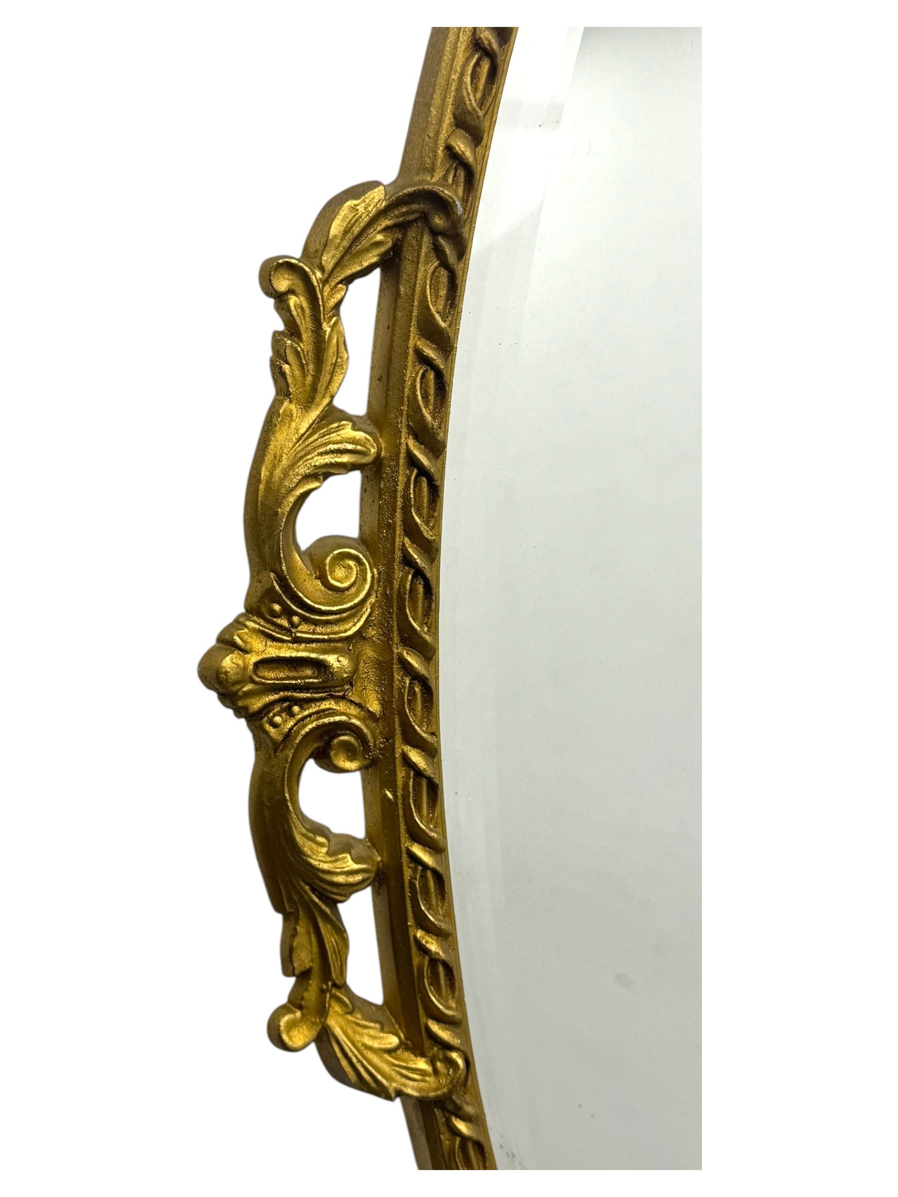 Oval gilt wall mirror, with bevelled edge plate within a moulded frame cast with acanthus scrolls and foliate decoration, pierced cartouche crest and apron, flanked by scrollwork handles
