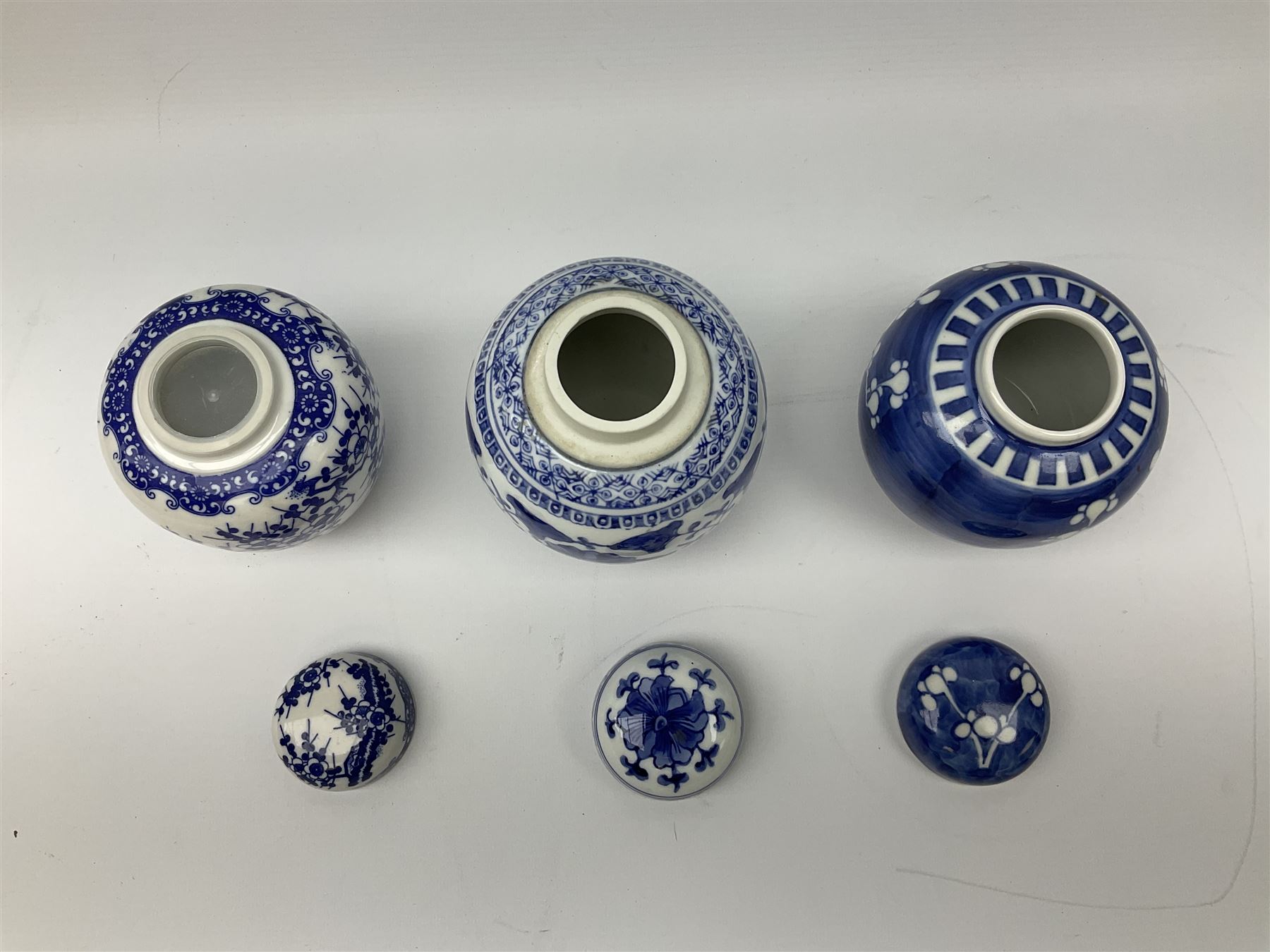 Six Chinese ginger jars, predominantly of blue and white design decorated with blossoming branches, all with lids, housed on various hardwood carved stands, some with character marks beneath