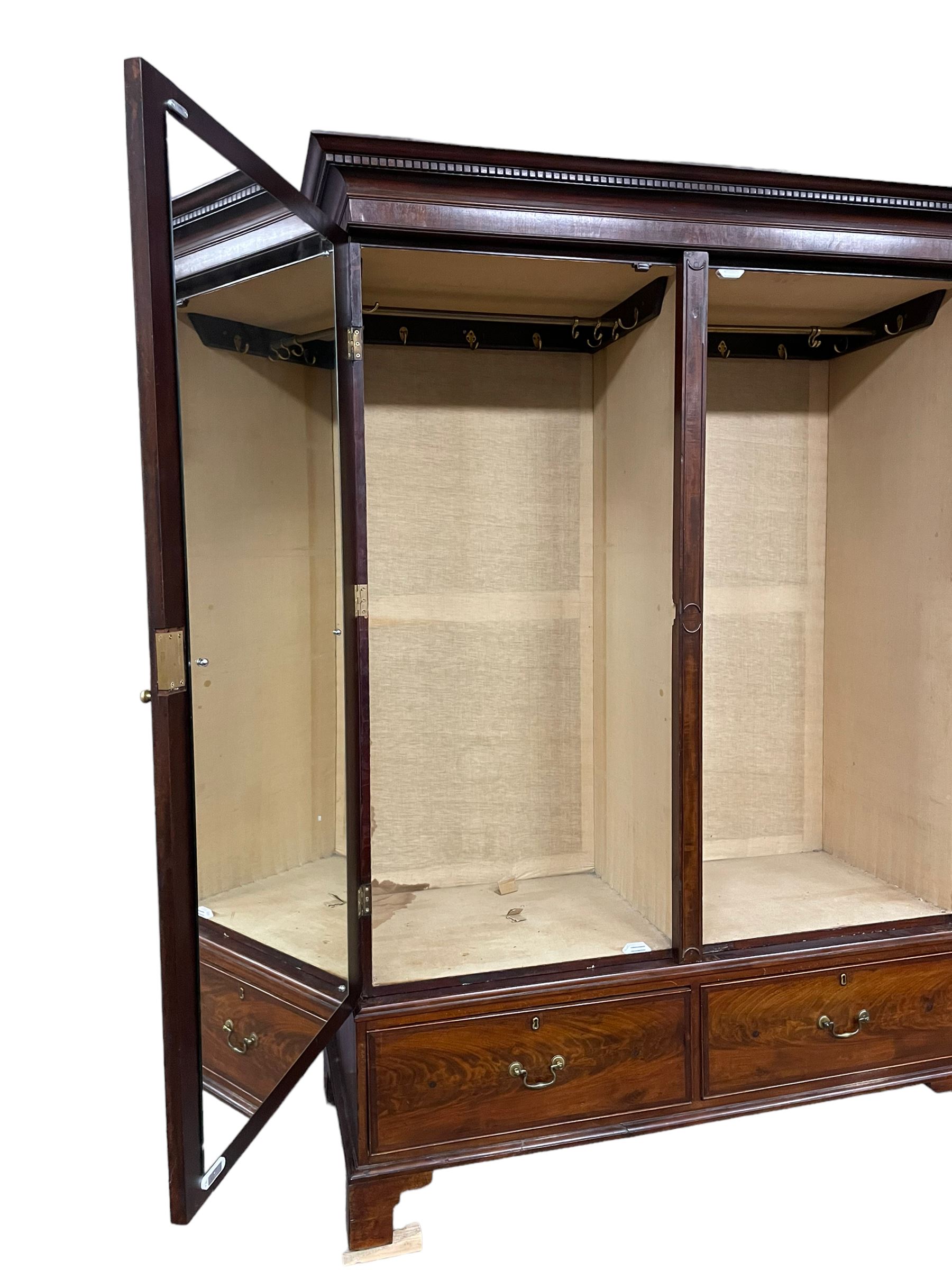 George III mahogany double wardrobe, the projecting cornice with dentil moulding over two panelled doors with mirror-lined interiors, enclosing hanging rails and brass hooks, the base fitted with two drawers, raised on bracket feet