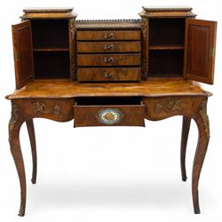 Late 19th-century Louis XV revival gilt bronze mounted and walnut Bonheur-de-Jour, rectangular-shaped serpentine form, with gilt bronze beading, frieze with two blind drawers and gilt bronze handles, centre drawer with large central serves style porcelain plaque, the elevated section with brass gallery above panelled cupboard doors also with serves style porcelain plaques and gilt bronze mounts, interior with single shelf, central section with four drawers each with gilt bronze handles, raised on slender cabriole legs fitted with gilt bronze rococo style masks and sabots