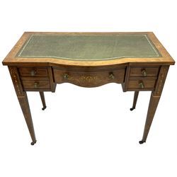 Edwardian inlaid rosewood writing desk, break bow-front with tooled and gilt green leather inset, fitted with five drawers, the central drawer with scrolling inlays, on square tapering supports inlaid with ribbons and flower heads, on brass and ceramic castors