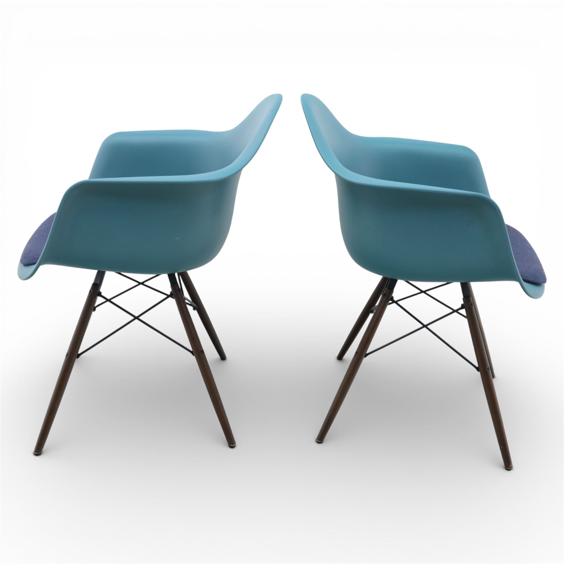 Vitra - Pair of Eames DAW armchairs, moulded plastic seats in teal with integrated armrests, blue upholstered seat cushions, supported on stained wooden dowel legs with black wire cross bracing