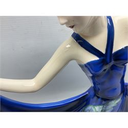 20th century American Goldscheider Art Deco figure, female in blue dress decorated with vines and grapes, holding up her skirts by the hem, on oval base, by Stefan Dakon, printed factory marks to base, impressed 8126 11 14, H40cm
