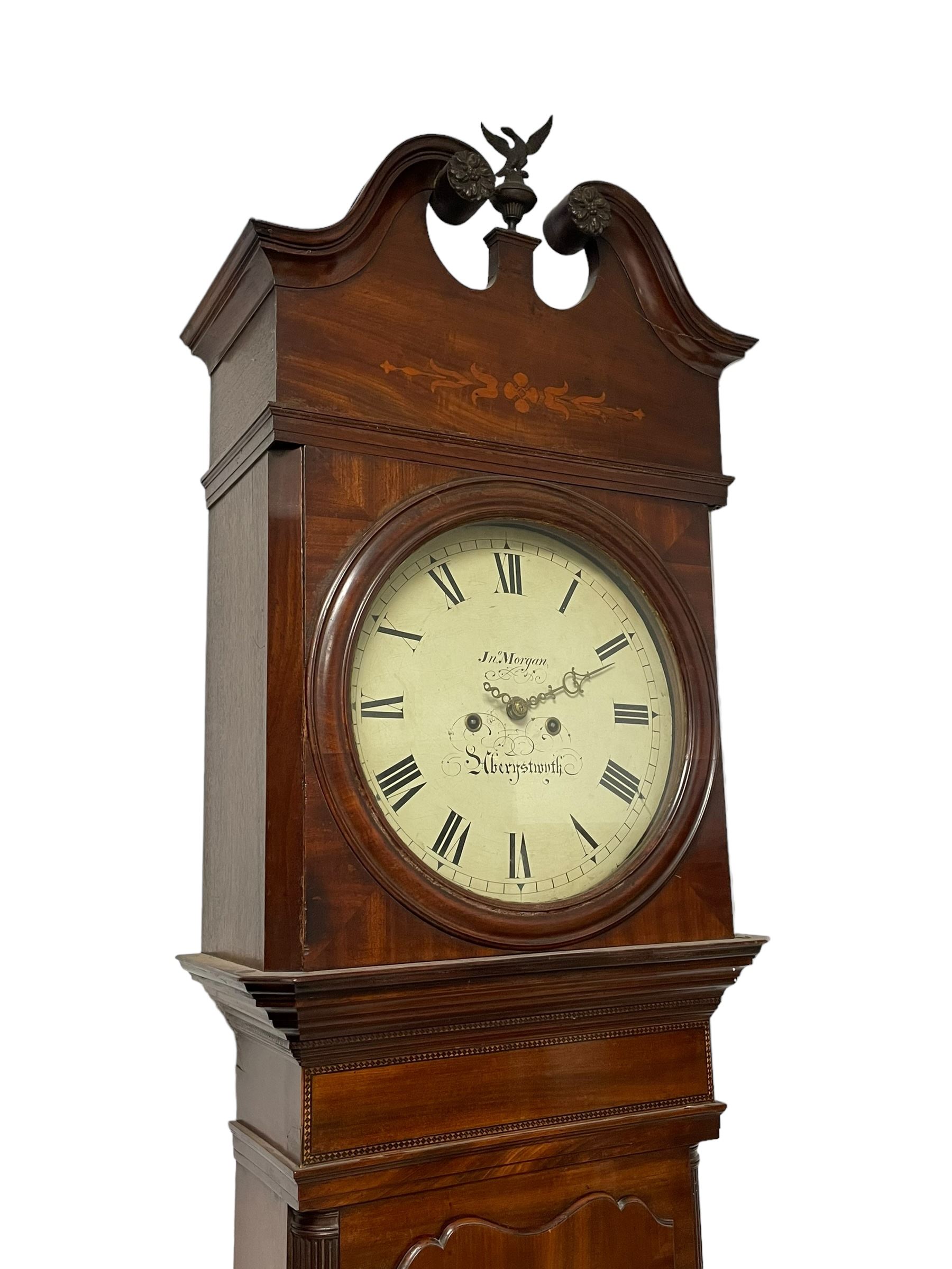 John Morgan of Aberystwyth - fine George IV mahogany 8-day longcase clock c1820, with a raised swan necked pediment, ball and eagle finial and deep inlaid frieze beneath, square hood door with a glazed circular wooden bezel and canted corners, long trunk with reeded quarter columns and a wavy topped door, rectangular plinth on bracket feet, circular painted dial with Roman numerals, minute track, makers name, and brass stamped hands, rack striking four pillar movement with a recoil anchor escapement, striking the hours on a bell. With weights and pendulum. 
John Morgan is recorded as working in Aberystwyth 1816-35. 