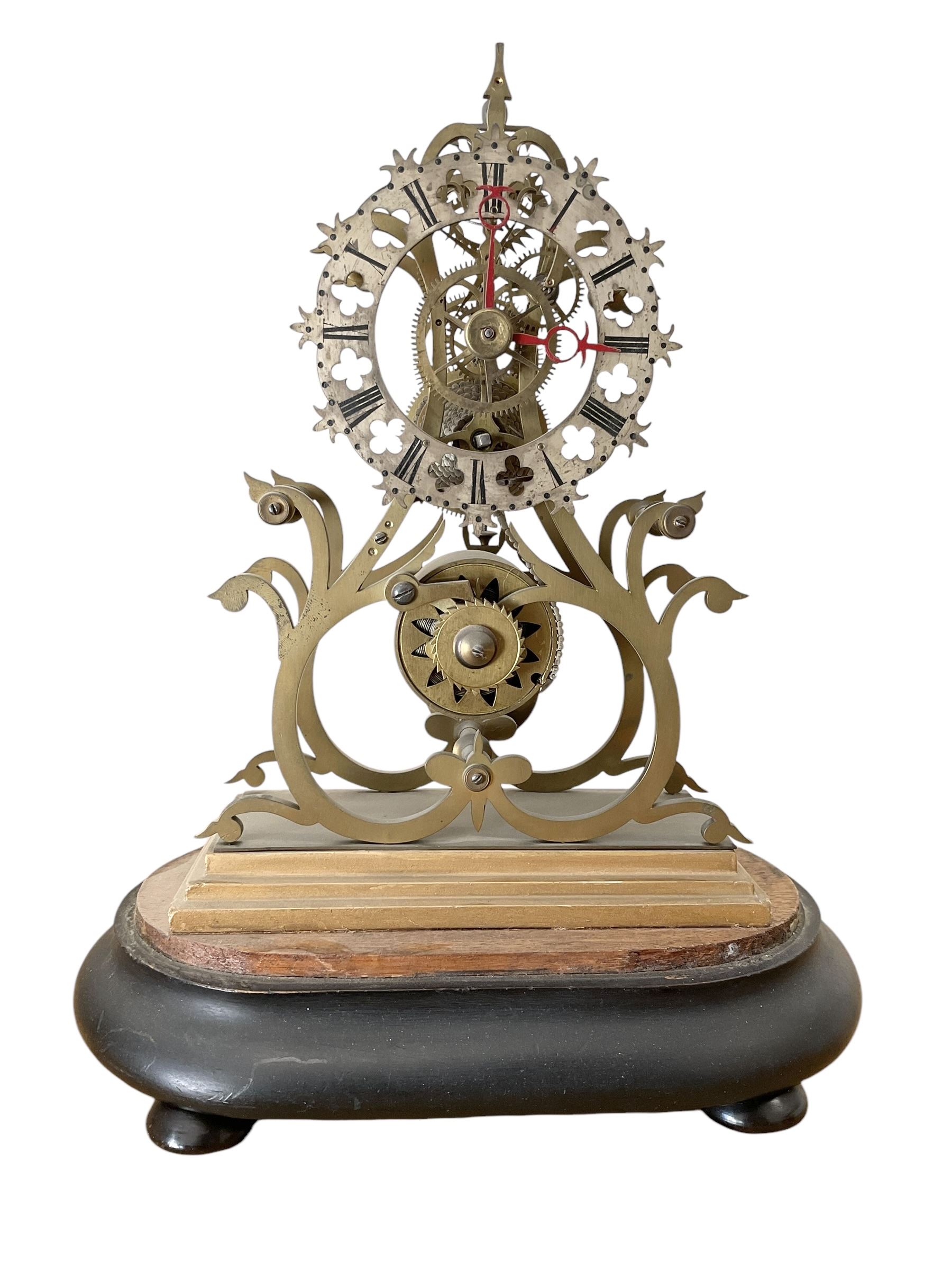 English-Late 19th century 8-day Skeleton clock on an oval ebonised base c1880, with pierced brass plates and silvered chapter ring, Roman numerals and gothic trefoil hands, chain driven five-pillar fusee movement and pierced mainspring barrel cap, timepiece movement with key and pendulum. 