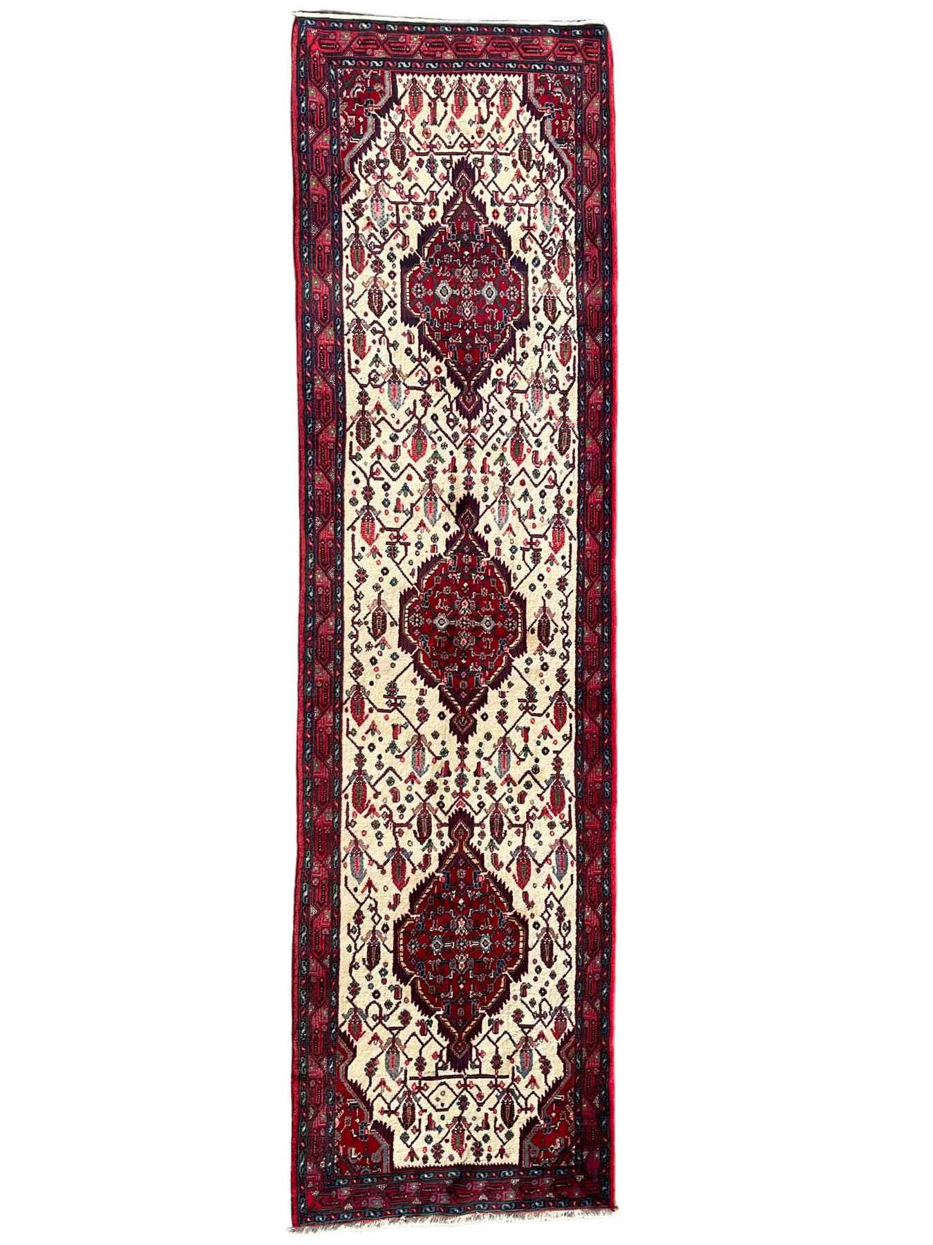 North West Persian Saveh crimson ground runner rug, the three lozenge pole medallions in an ivory field, surrounded by stylised plant motifs, the guarded border decorated with repeating geometric patterns