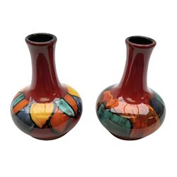 Two Poole pottery baluster vases, brightly decorated on red ground H15.5cm