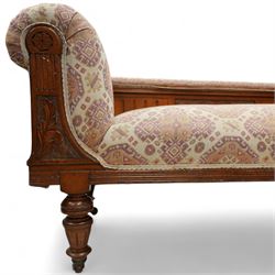 Late Victorian walnut chaise longue, upholstered in geometric patterned fabric, the scroll end and padded back above carved side panel with foliate and roundel motifs, shaped seat rail on turned front supports with ceramic castors