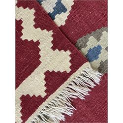 Handwoven wool Kilim rug of rectangular form with cream fringe, the red ground decorated with repeated multicoloured hexagonal medallions within a cream stepped border
