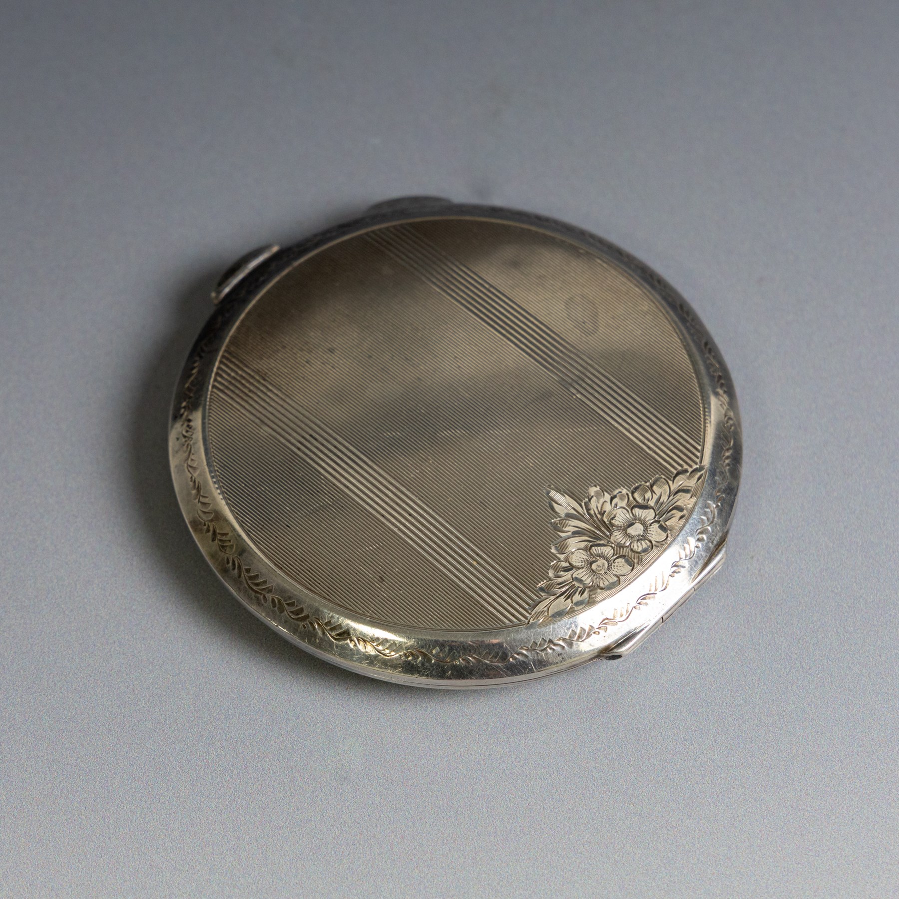 Two silver compact mirrors, comprising a Kigu powder compact with engine turned decoration and a compact mirror with floral decoration, both hallmarked