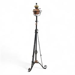 Early 20th century converted oil lamp standard, with copper reservoir and brass burner mount, later wired for electricity, on wrought iron tripod stand with scroll and twist ornamentation