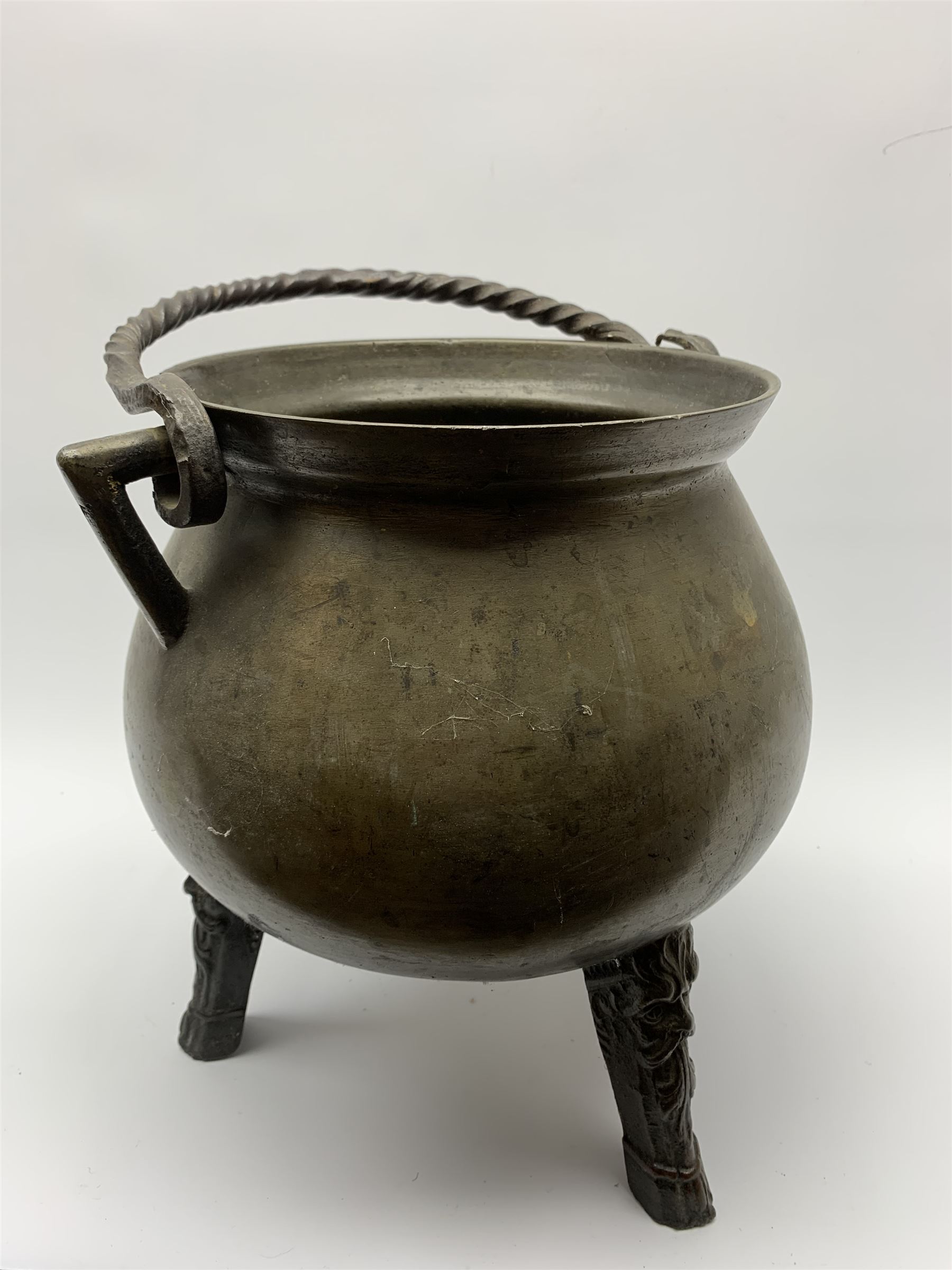 17th century bronze cauldron, probably German or Austrian, of bellied form with twin angular handles supporting a twisted handle, upon three splayed zoomorphic bearded mask feet, not including handle H30cm, rim D22cm