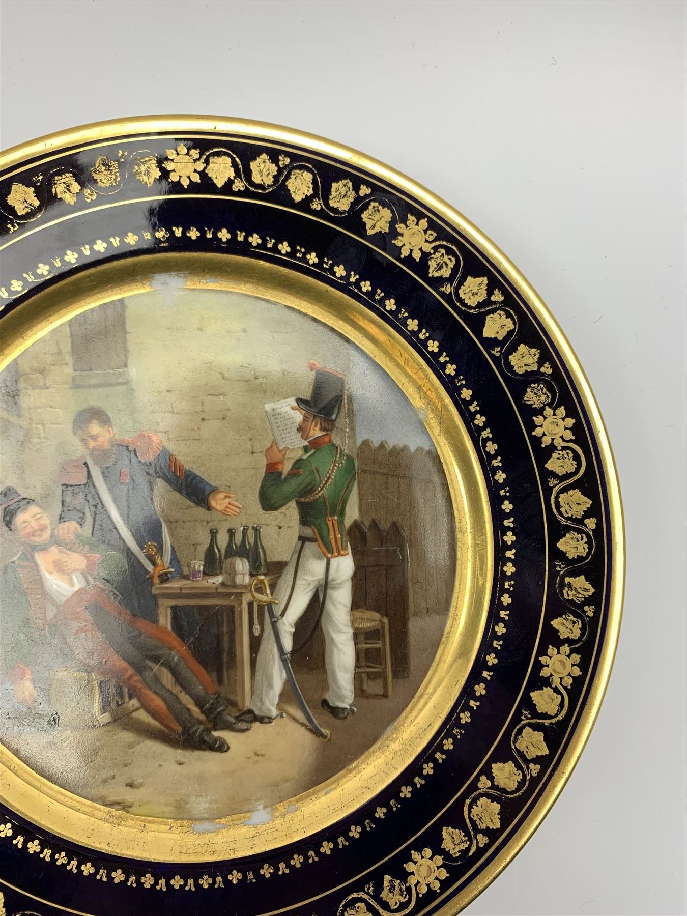 19th century Rihouet Paris porcelain cabinet plate, decorated with a central panel illustrating three French soldiers around a bottle laden table, one surveying a note, within a dark blue gilt detailed border, with French inscription verso, and red printed mark Rihouet Rue de la Paix A Paris and green fish mark, possibly for Perche, D23cm 



