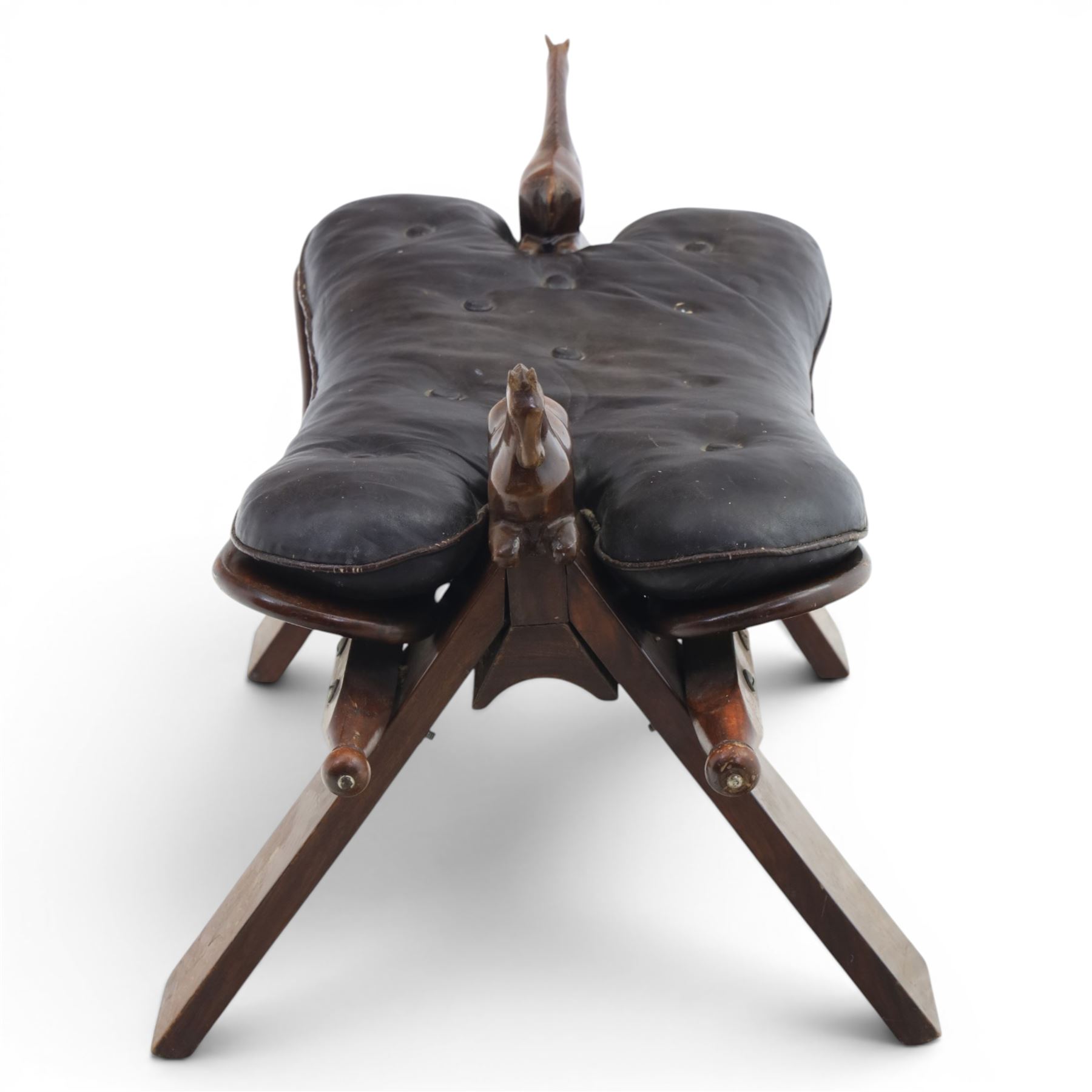 20th century saddle stool, wiht black leather seat, surmounted with carved horses, on an X-frame base with brass inlay
