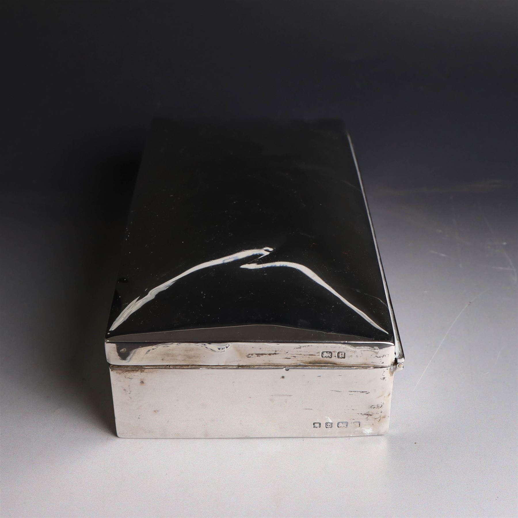 Two silver cigarette boxes, comprising early 20th century plain rectangular example with compartmentalised softwood interior, hallmarked Birmingham 1914, maker's mark indistinct, and an early 20th century example with engine turned decoration and engraved initials to cover, hallmarks worn and indistinct, largest H4.5cm, W21cm