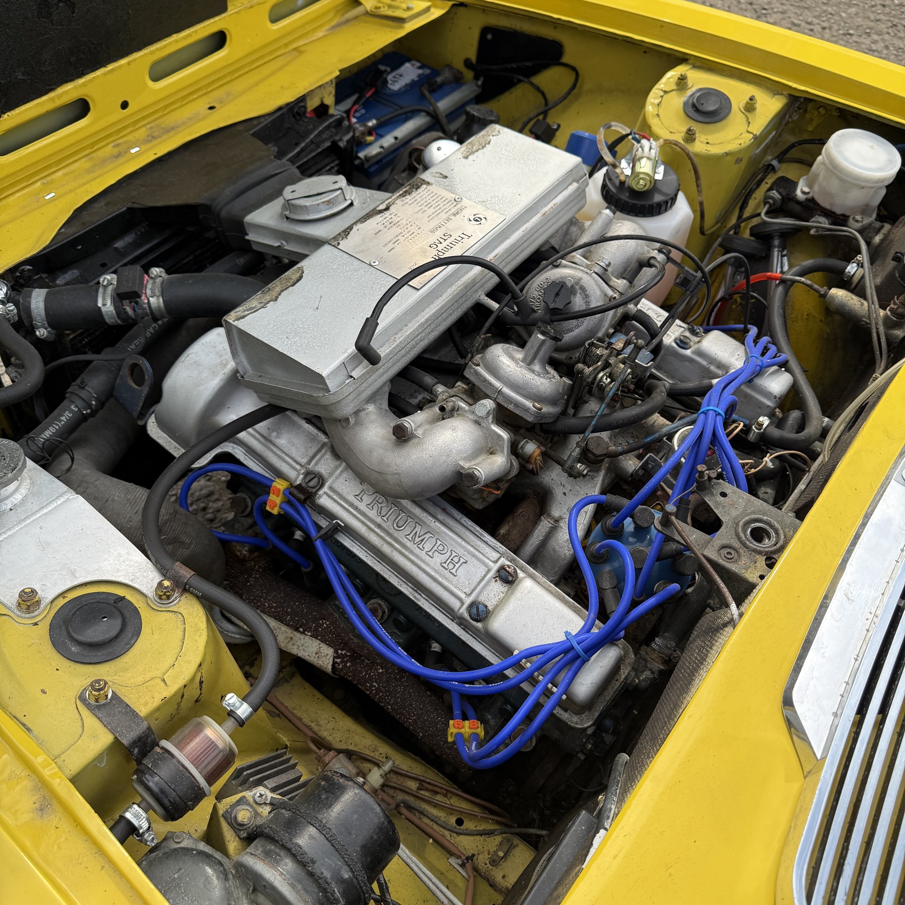 1973 Triumph Stag Mk II 3.0 V8 Manual with Overdrive

Registration: FTV 859L
Date of first registration: 8th March 1973
Recorded mileage: approximately 50,000 miles
Engine: 2,997cc petrol V8
Transmission: four-speed manual with overdrive

An attractive manual-overdrive example of Triumph’s celebrated V8 grand tourer, finished in yellow and supplied with both a removable hardtop and folding soft top.

The car has been the subject of extensive restoration and mechanical work, supported by a large history file containing invoices, notes and photographs documenting the work undertaken. The accompanying records indicate that the engine was rebuilt at approximately 36,000 miles, including re-boring of the block, checking and machining of the top faces, and steam cleaning following machining.

Further work and replacement parts are understood to include an upgraded radiator, electric cooling fan, Stag Webber header tank kit, complete set of cooling hoses and clips, fuel pump and filters, alternator, distributor cap, HT leads, spark plugs, front brake calipers and hoses, rear brake cylinders, tyres, front lights and LED bulbs. Various seals, interior trim items and seat components have also reportedly been renewed.

The car is believed to have been dry-stored from 1994 until 2017, with a substantial programme of recommissioning and improvement subsequently undertaken between 2017 and 2023. The history file also includes earlier MOT certificates dating from 1988 to 1994.

Offered with its V5C, hardtop, soft top, extensive restoration and maintenance history, photographic record and a quantity of useful spare parts, including a new dashboard veneer set.