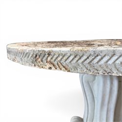 Weathered cast stone garden table, circular top etched with central floral medallion, the edge with repeating chevron motifs, raised on a quadriform S-scroll pedestal with stepped and chevron carved base