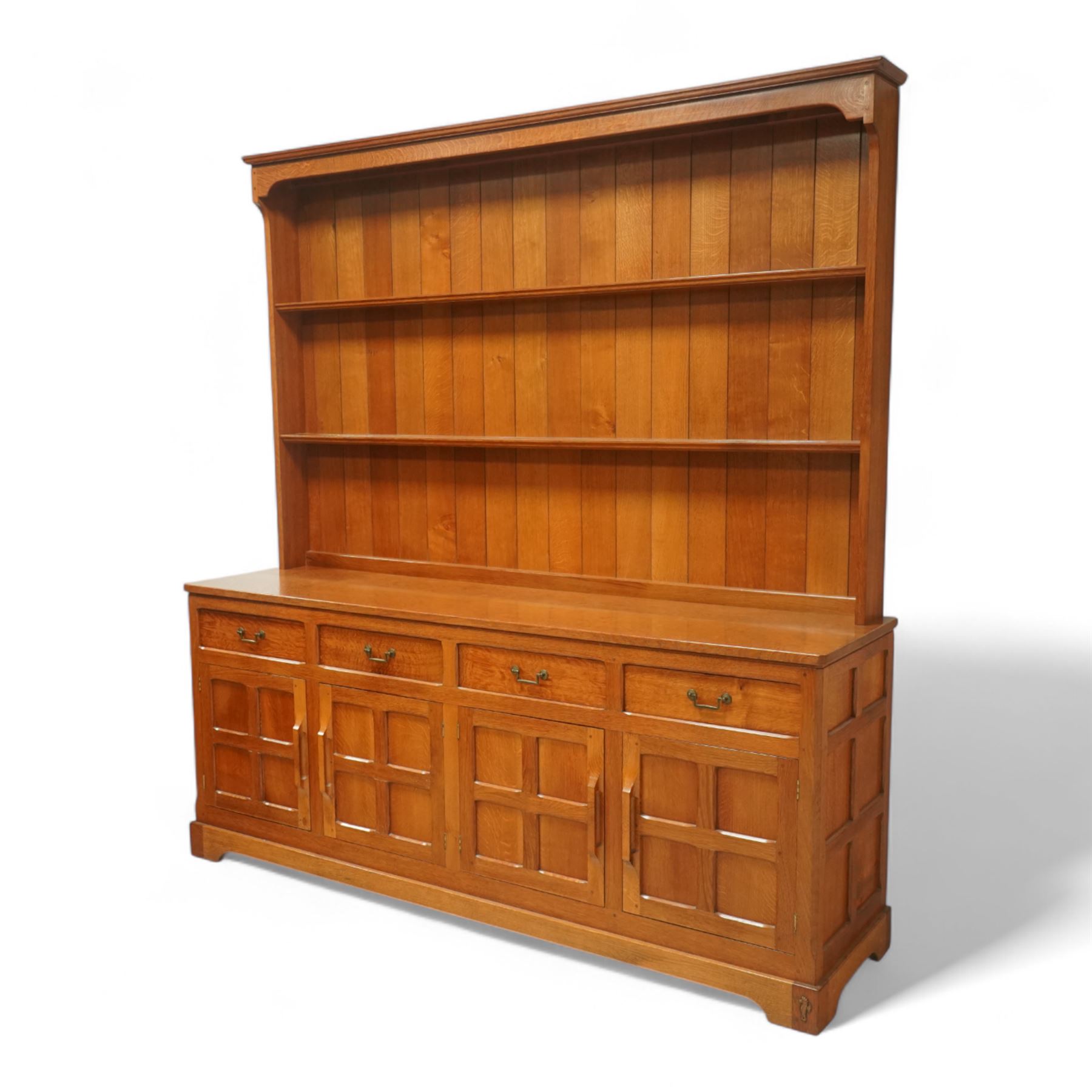 Seahorseman by Shaw & Riley - Yorkshire oak Welsh dresser, the dresser rack of rectilinear form with plain frieze and projecting moulded edge above two shelves with central shallow groove, the base section fitted with four drawers and a fitted cutlery drawer containing cutlery, above four panelled cupboard doors with geometric mouldings and carved sculpted handles, interior with single shelf and sides with geometric mouldings raised on a shallow plinth base with shaped bracket feet, with signature Seahorse carving from the workshop from the workshop of A. Shaw & Riley Ltd, Hessay