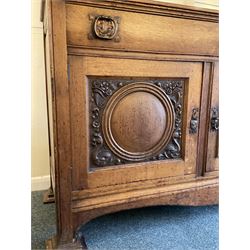 Late 19th century Arts & Crafts period oak mirror back sideboard, shaped bevelled mirror back carved with foliate scrolls and flower heads, down swept supports with elongated club-shaped uprights, moulded rectangular top over two drawers and three cupboards, the drawer fronts with copper handles decorated with sailing ships, panelled doors carved with mythical beasts, flowerheads and foliage, on moulded block feet