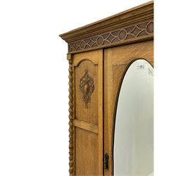 Early 20th century oak wardrobe, projecting cornice of blind fret-work frieze, oval bevel edge mirror door, half spiral turned pilasters, drawer to base with mouldings, on turned bun feet