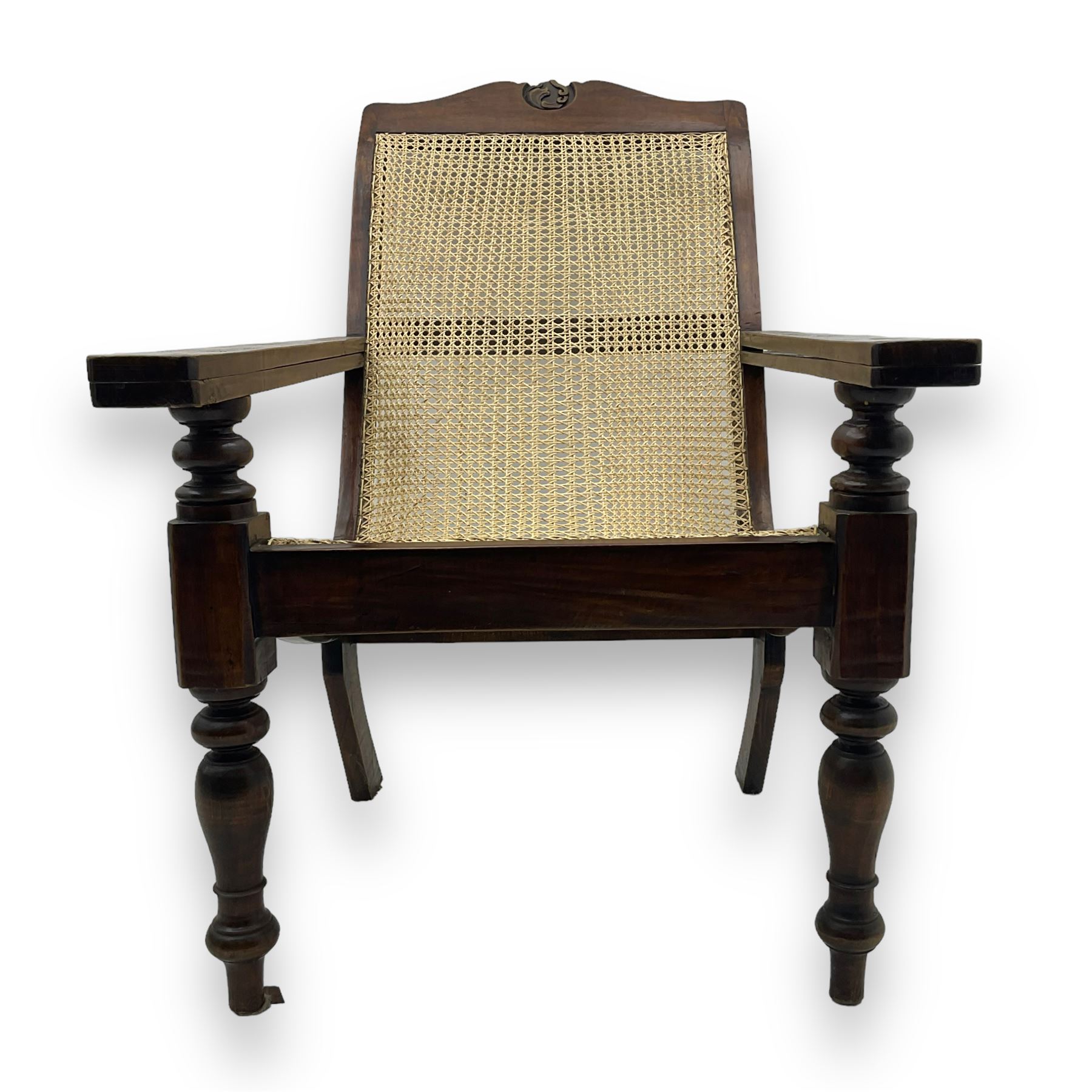 Late 19th century caned plantation chair, shaped top rail with carved central motif over caned back and seat, extending armrests, on turned front supports