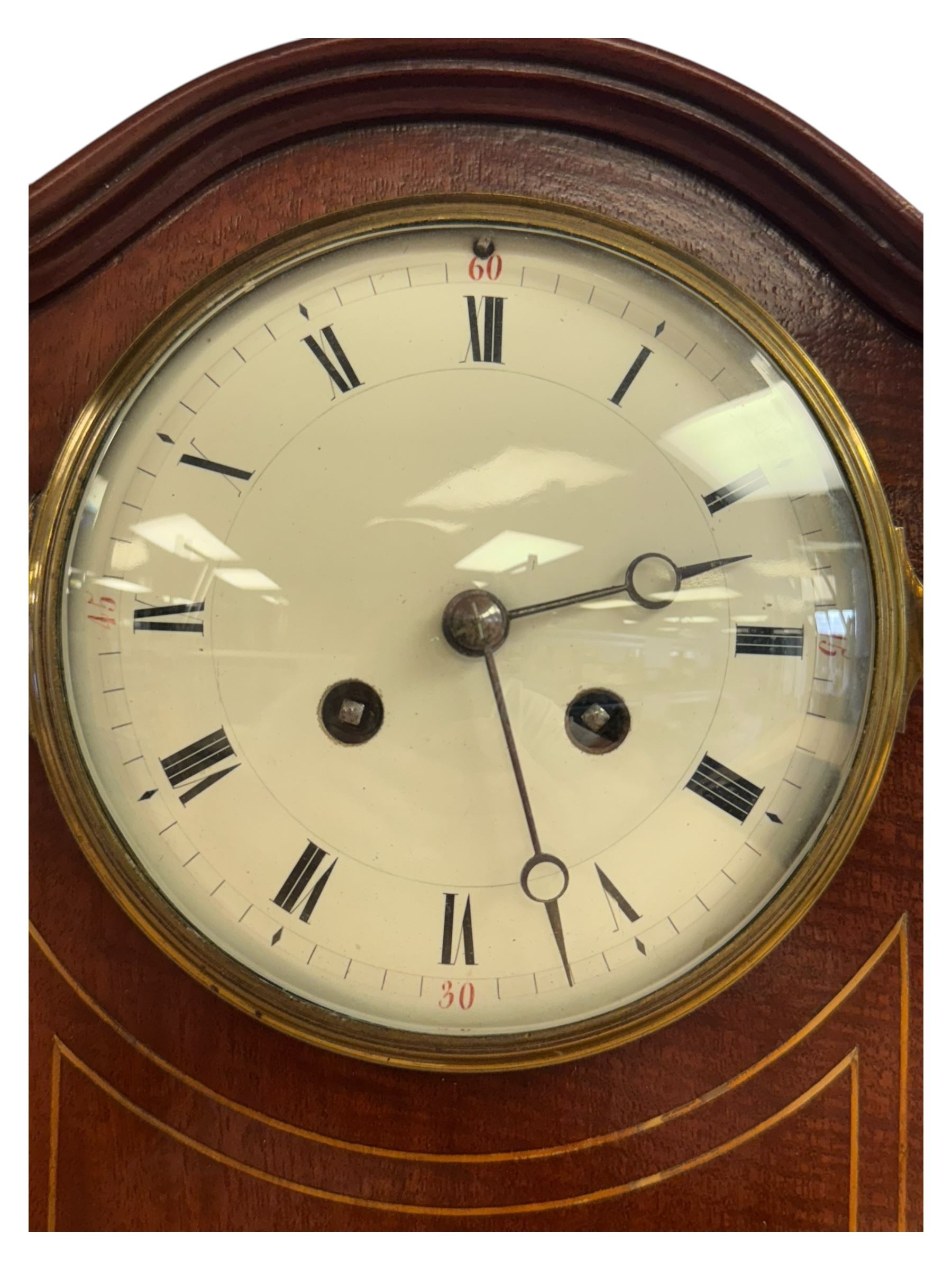 Edwardian-French 8-day mantle clock in a mahogany case with satinwood inlay, on a narrow plinth raised on ball feet, enamel dial with Roman numerals and steel moon hands, rack striking movement, sounding the hours and half hours on a gong. With pendulum and key.