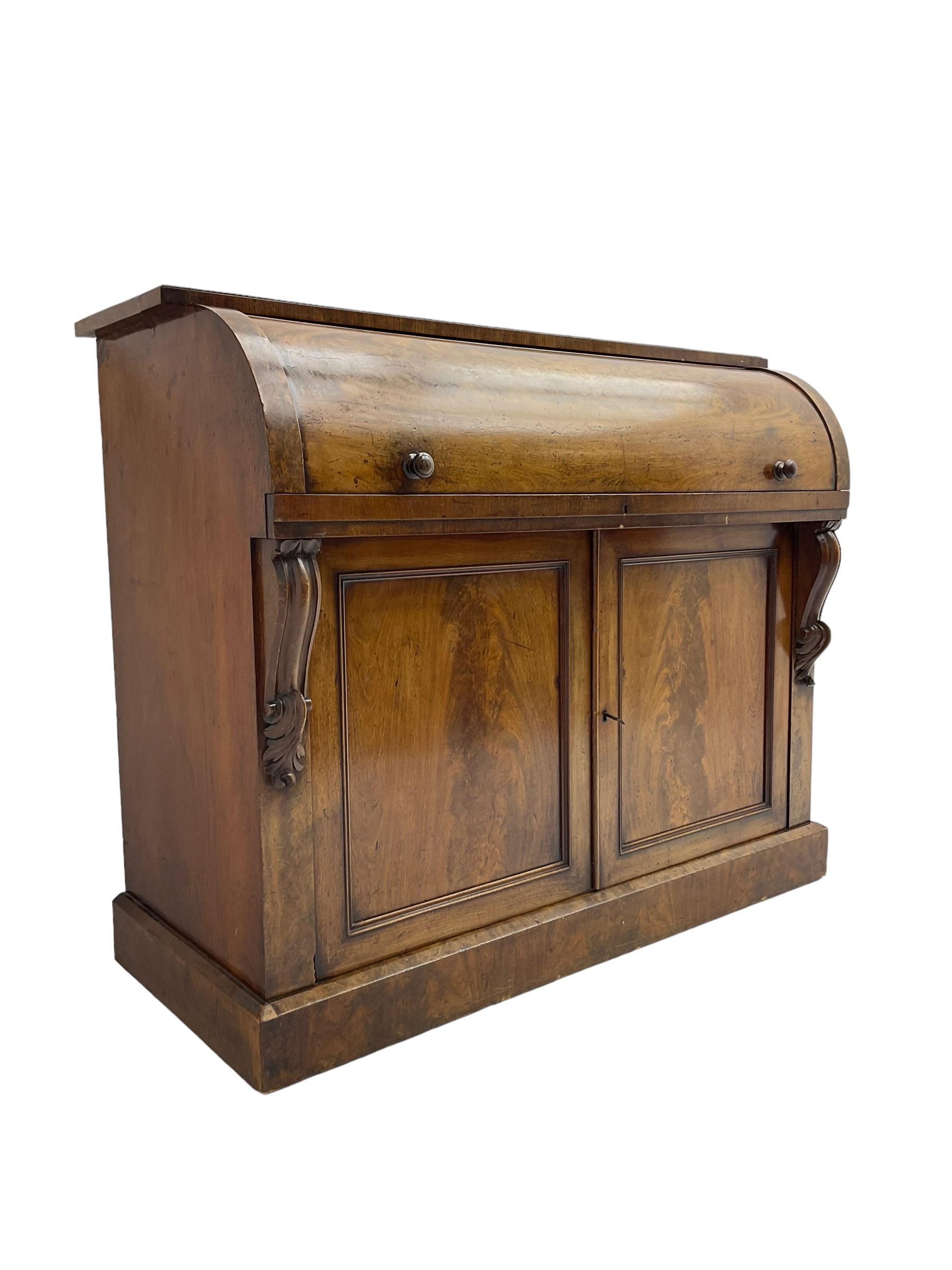 Victorian mahogany roll-top writing desk, top concealing fitted interior with pigeonholes and three drawers, the trisector inset writing surface with writing slope, base fitted with panelled cupboard enclosing single shelf, decorated with scrolled corbels