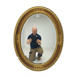 Oval wall mirror, in gilt frame decorated with scrolled foliate and scalloped outer edge, bevelled plate 