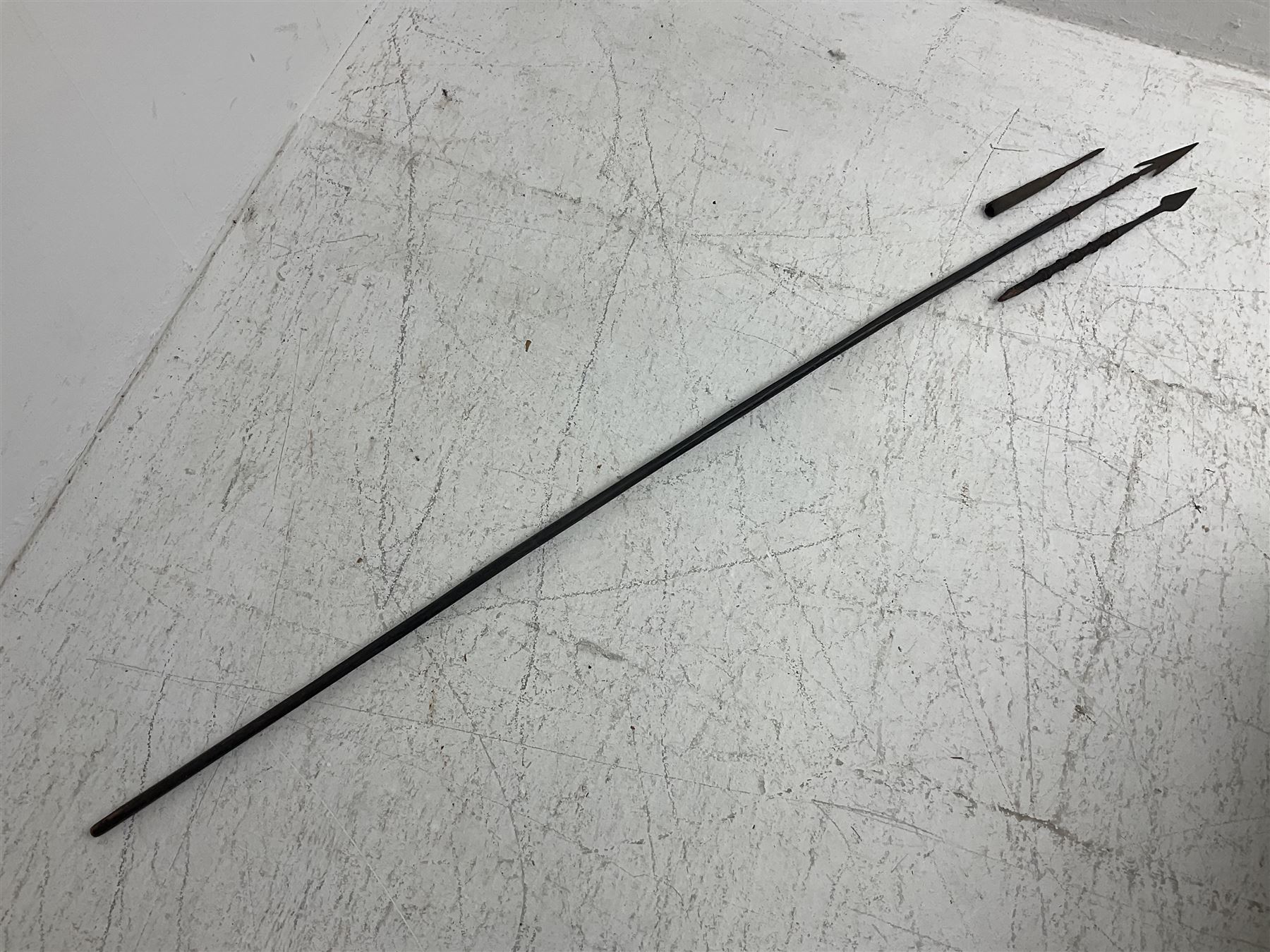 Native hand forged iron fishing spear, the V-shaped head with barbed neck and hewn haft L171cm; and two other hand forged iron spear heads, one with remains of copper bound haft (3)