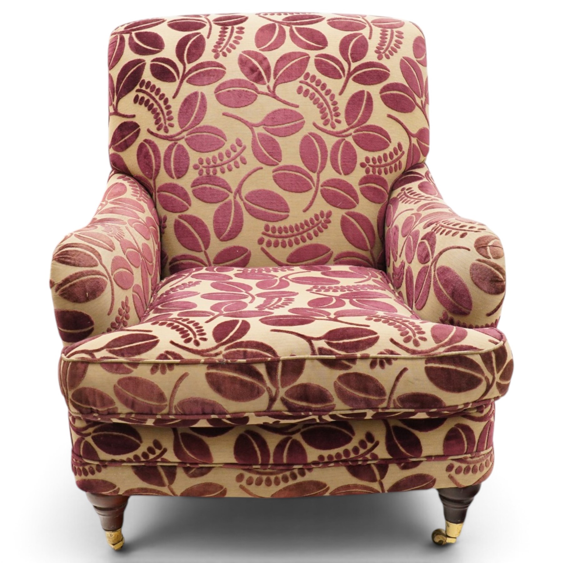 Traditional Howard shape armchair, rolled back and arms over deep seat, raised on turned supports with brass cups and castors, upholstered in plum foliate patterned fabric with loose seat cushion