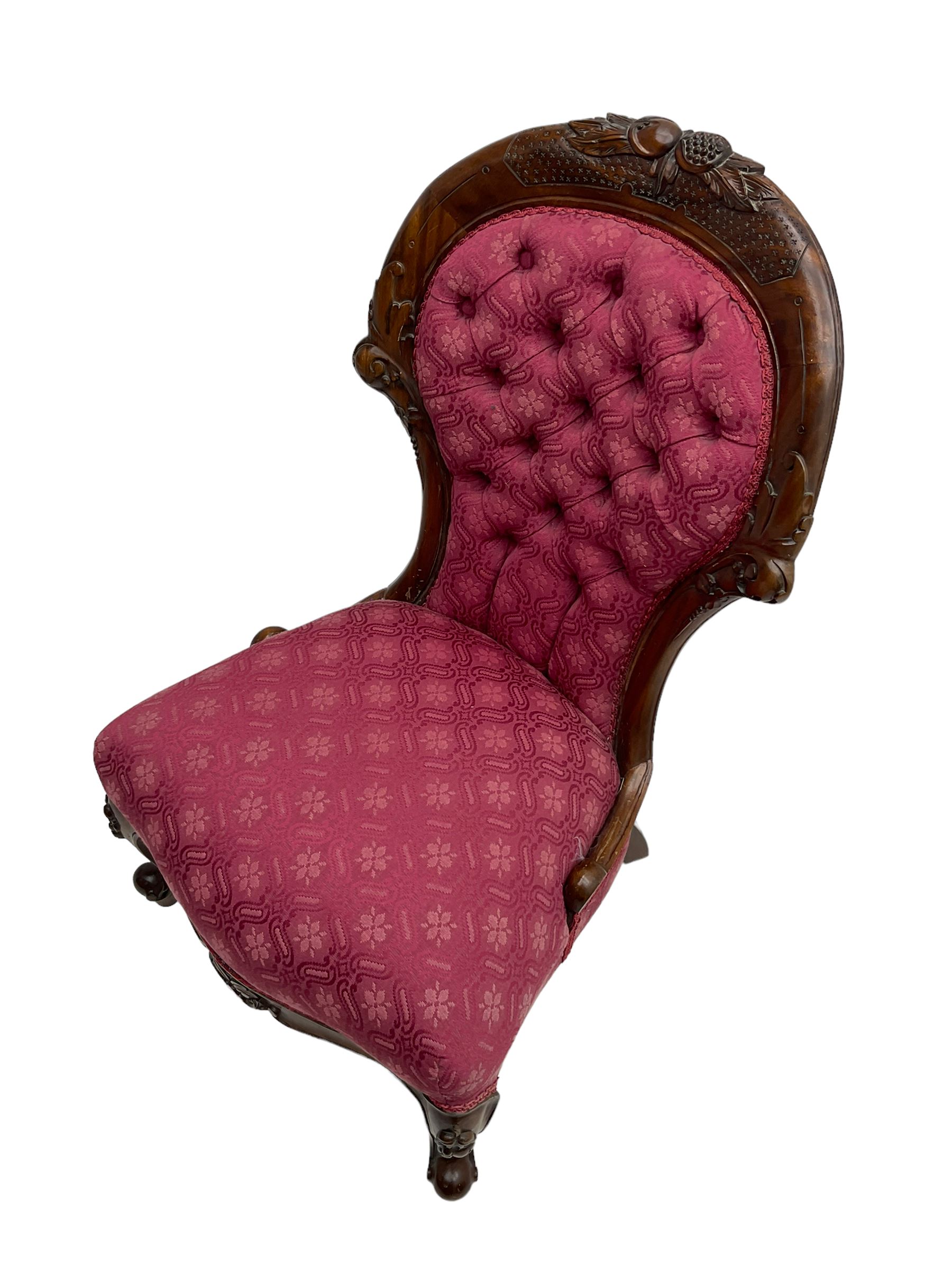 Victorian style mahogany framed nursing chair, the cresting rail carved with fruit and foliage, upholstered in red patterned fabric with buttoned back, on cabriole supports with scrolled terminals