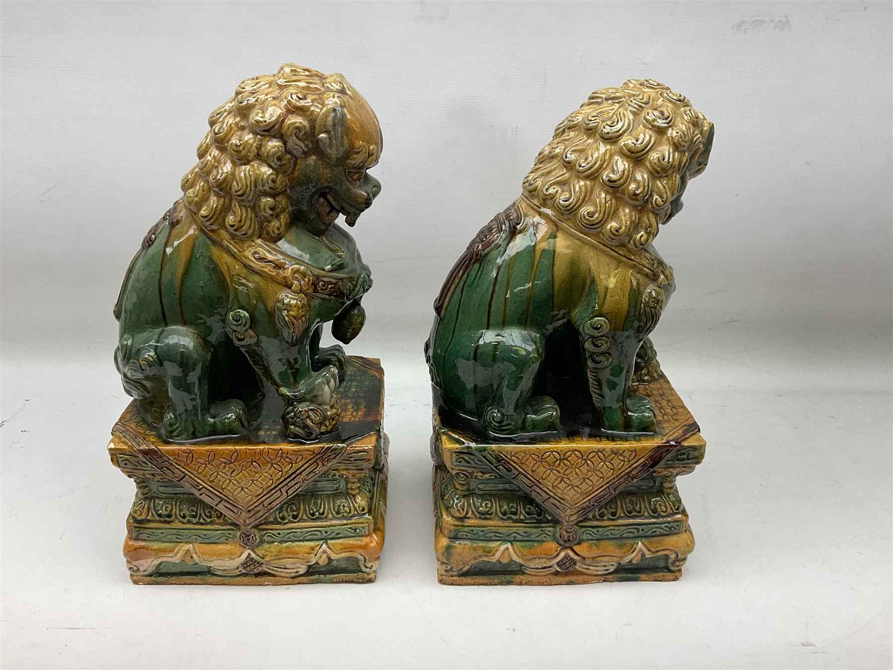Pair of Chinese Temple Lions or Dogs of Foo, modelled in seated post, one with one front paw resting upon a ball, the other upon a cub, each upon stylised plinth base, H44cm