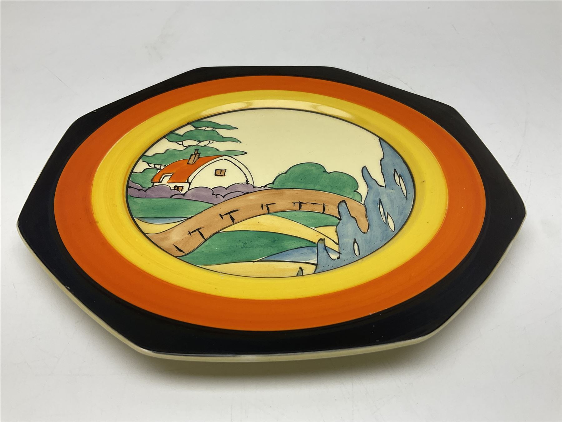 Clarice Cliff Bizarre for Newport Pottery Orange Roof Cottage pattern plate, circa 1932, hand painted with a stylised cottage and bridge landscape with yellow, orange and black banding, black printed mark beneath, D22cm 