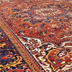 North West Persian Ahar hand-knotted carpet, red field with large central angular star medallion with stepped outlines and radiating geometric motifs surrounded by stylized floral and serrated leaf forms, enclosed by a deep blue main border decorated with angular palmettes and rosettes flanked by multiple guard stripes, with cotton fringe ends 