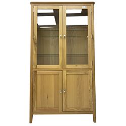 Contemporary light oak display cabinet on cupboard, fitted with two glazed doors enclosing two adjustable glass shelves with light fittings to the top, over panelled cupboard concealing single shelf, on square supports