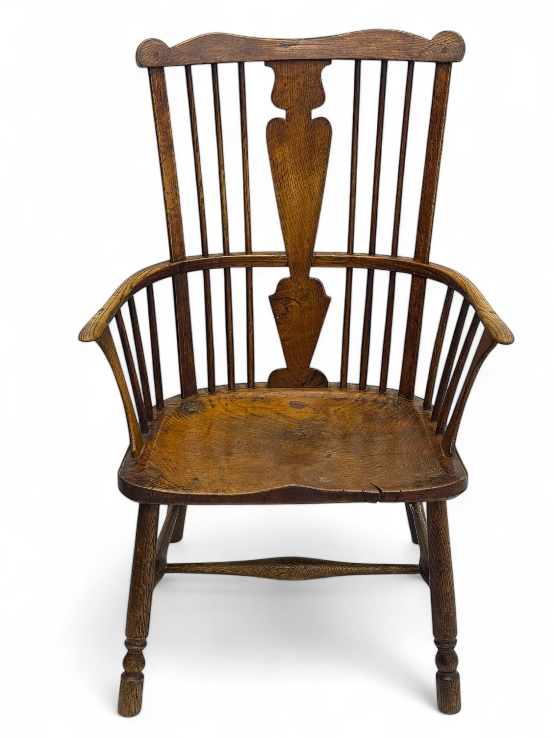 Early-to-mid 19th century elm and ash high-back Windsor armchair, central vase-shaped splat flanked by slender vertical spindles, outward-curving arms, shaped and dished saddle seat, raised on turned and splayed supports united by H-stretcher